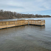 Open water season A lake with a wooden dock and trees along the shoreline.